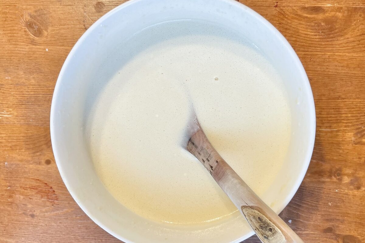 Crepe batter in a white bowl with a wooden spoon.