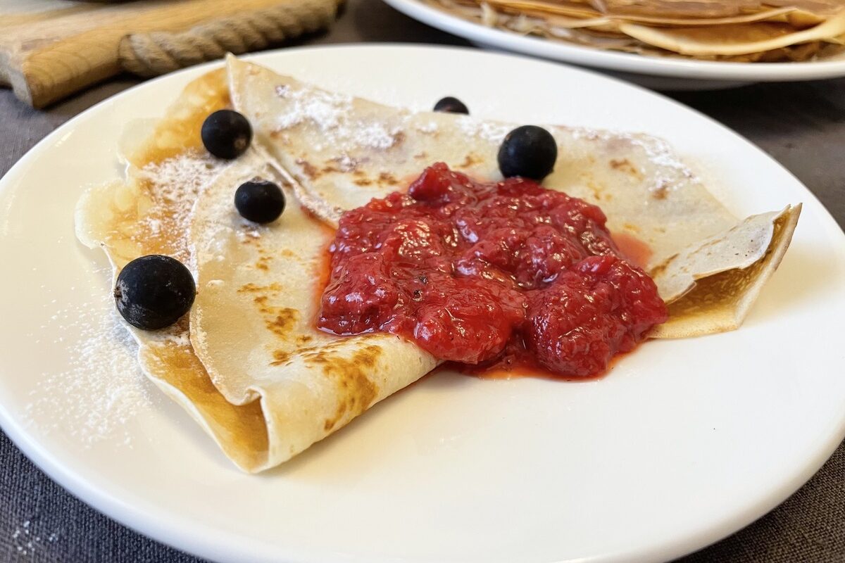 A beautifully served crepe with strawberry jam and berries.