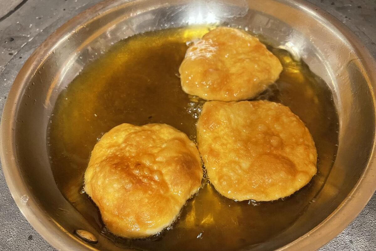 Dough snacks deep frying on a stainless steel pan.